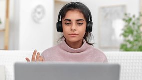 Modern skilled Asian young woman in headphones talking online video call use laptop working remotely at home. Cute smart female internet distance meeting on computer e learning education teleworking