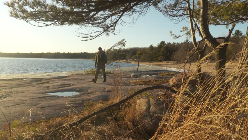 Hiker crossing shorling of Killbear Provincial Park on a cold early spring sunset