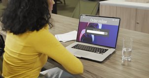 Biracial woman at table using laptop, online shopping for gamepads, slow motion. Retail business, sale and digital interface digitally generated video.