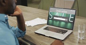 African american man at table using laptop, online shopping during sale, slow motion. Retail business, sale, communication and digital interface digitally generated video.