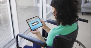 Biracial woman sitting in wheelchair using tablet for online shopping, slow motion. Retail business, sale, disability and digital interface digitally generated video.