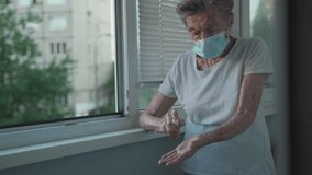 Elderly woman in a medical mask washing hands with alcohol gel or antibacterial soap sanitizer standing by the window in a nursing home. Hygiene during the COVID-19 coronavirus pandemic. - Powered by Shutterstock - Get 15% off with code: PIKWIZARD15
