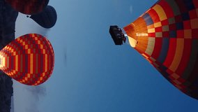 Vertical video. It's still dark, and stars are visible in the sky, while the multicolored hot air balloons with people in the baskets are already in the air.