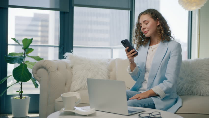 Excited stylish woman celebrate online victory on sofa at home. Model holds cellphone check e-mail app on phone feels excited looking happy by lottery win. Winner enjoy moment of success, bet concept Royalty-Free Stock Footage #1110038469