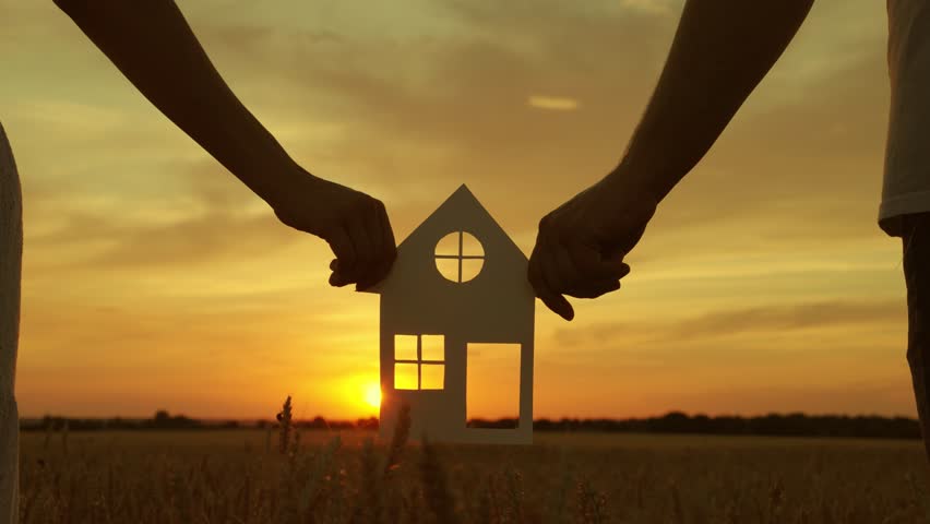 Symbol of house, happiness. Family hands are holding paper house at sunset, sun is shining through window. Family Home, Real estate insurance. Concept of building house for family. Dream to buy house Royalty-Free Stock Footage #1110040873
