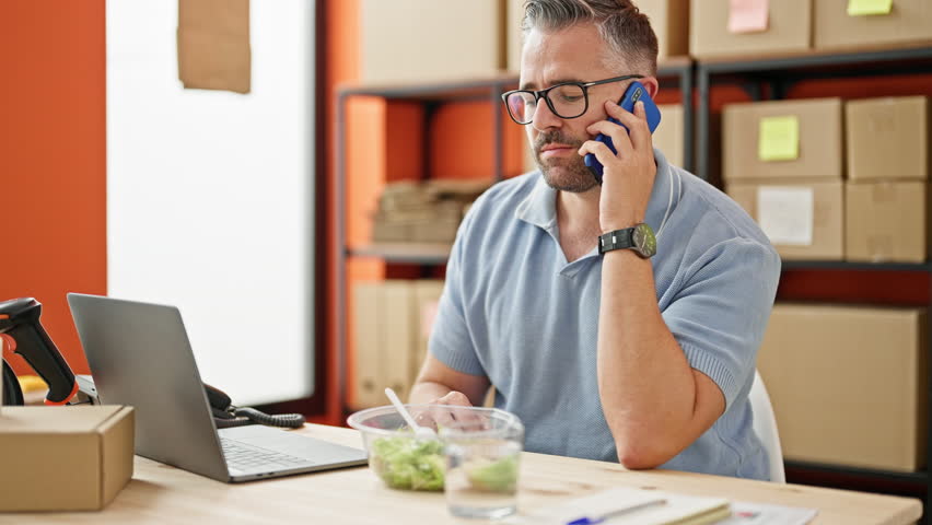 Grey-haired man ecommerce business talking on smartphone drinking water at office
