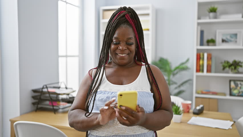 Smiling african american woman boss gives a thumb-up gesture while working on her phone in the office, embodying elegance and success in the midst of her professional duties Royalty-Free Stock Footage #1110043485