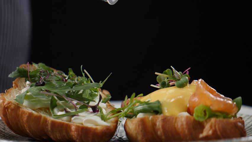 Serving breakfast with croissant sandwich, green salad and tomato being poured with cheese sauce. Slow motion. Baker prepares croissant dish for serving at restaurant. Chef pouring sauce on fresh