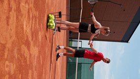 vertical video a young coach teaches a beginner girl to play tennis, practice movements with racket practice with a ball on a tennis court