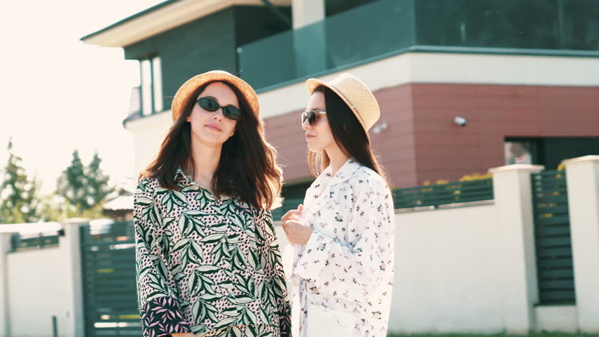 Two young beautiful smiling hipster woman in trendy summer sundress. Carefree women posing in street in hats. Positive models having fun and hugging at sunset outdoors. Cheerful and happy