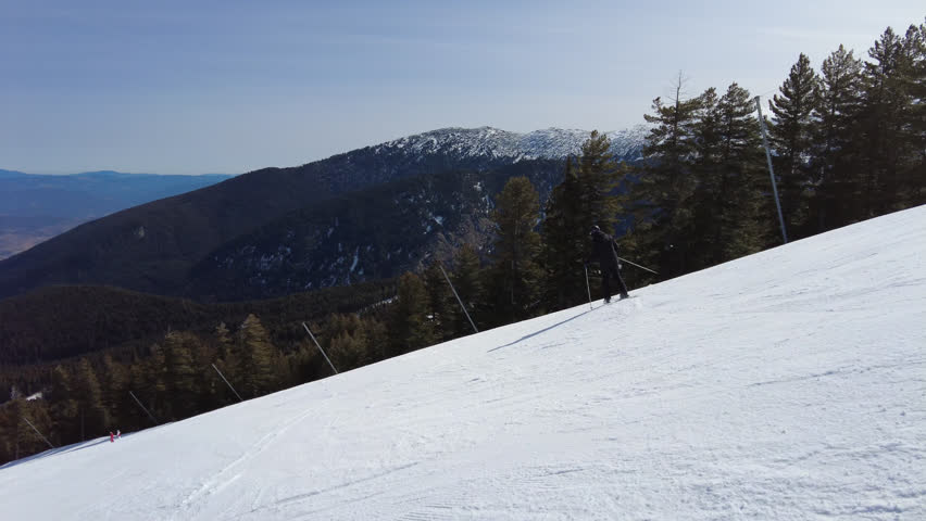 Male skier dressed in black, man skiing down a tree lined snowy mountain piste or slope on fresh snow 4K Stabilised Video Clip