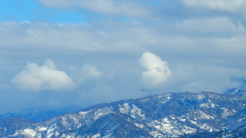 Mountains With Clouds Running Opposite Direction On Blue Sky. Snow-Covered Hills Of Mountains. Timelapse.