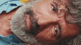 Vertical video, Close-up portrait, happy elderly grey-haired bearded man wearing blue shirt, looking camera with smile, isolated on orange background in studio - Powered by Shutterstock - Get 15% off with code: PIKWIZARD15