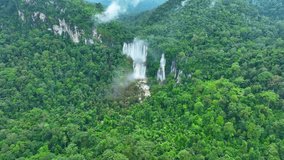 A breathtaking hidden gem, a large waterfall nestled within the lush embrace of a tropical rainforest jungle. The dense, emerald canopy showcases the raw power of nature, as captured by a drone's eye.