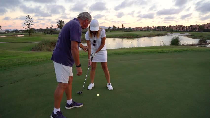 Older man giving golf lessons to an older woman on a golf course. She takes a shot at the ball - Powered by Shutterstock - Get 15% off with code: PIKWIZARD15