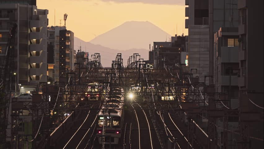 Train traveling on railway track during sunset in Japan, Mt. Fuji view in background. Japanese transportation system, Asian commuter lifestyle, Asia tourism concept | Shutterstock HD Video #1110063539