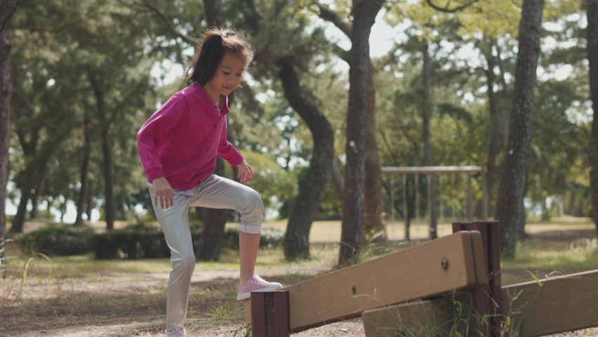 Asian girl kid, alone in her summer activity with playful exploration and determination by walking with balance onto a wooden balance beam in beautiful forest park in summer sunlight. Royalty-Free Stock Footage #1110065821