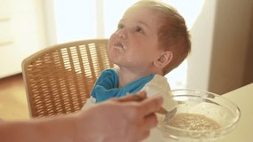 mother feeds porridge to her son. happy family healthy food concept. the boy little son eats porridge with a spoon soiled in his face. child dirty dirty funny lifestyle eating porridge himself video