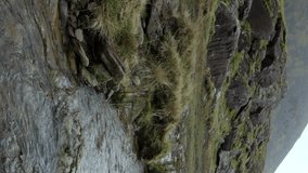 A clear mountain stream flowing amid rocky surroundings, set against a backdrop of clouds. Vertical video, pan.