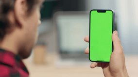 Close Up of Phone with Green Screen Mock Up Display In Male Hands. Man Sitting In Office Browsing Internet , Watching Content, News, Financial Reports on Phone