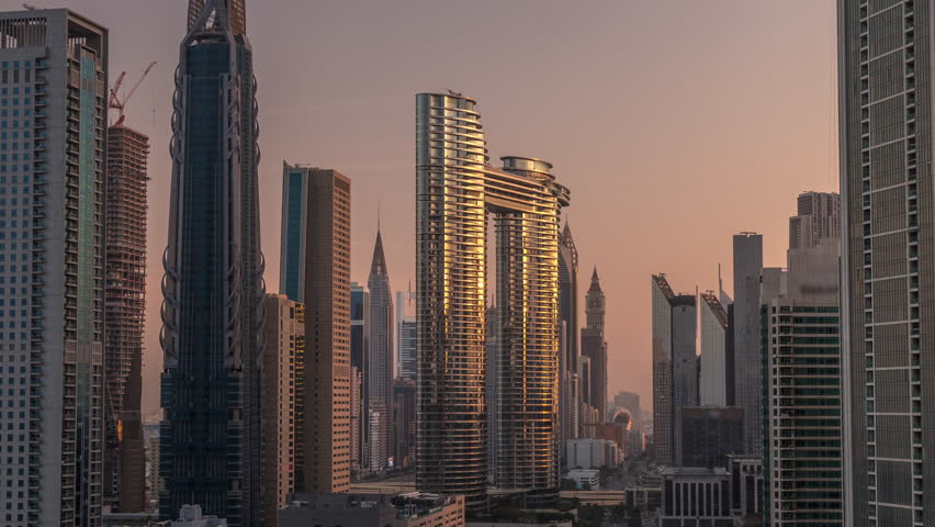 Futuristic towers and skyscrapers with traffic on streets in Dubai Downtown and financial district. Urban city skyline aerial morning timelapse during sunrise. Warm light and sun reflected from glass