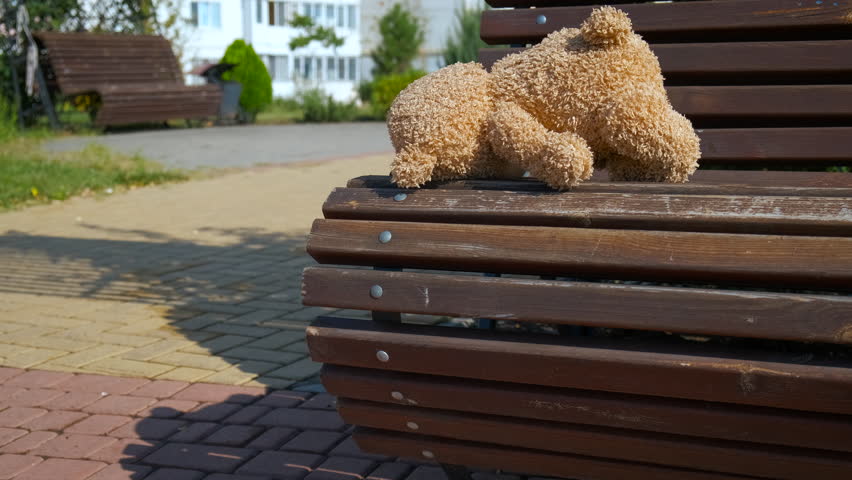 Left teddy bear on bench in park. A little teddy bear waiting for child on the park bench. A concept of kidnapping problems in the city. Royalty-Free Stock Footage #1110078991