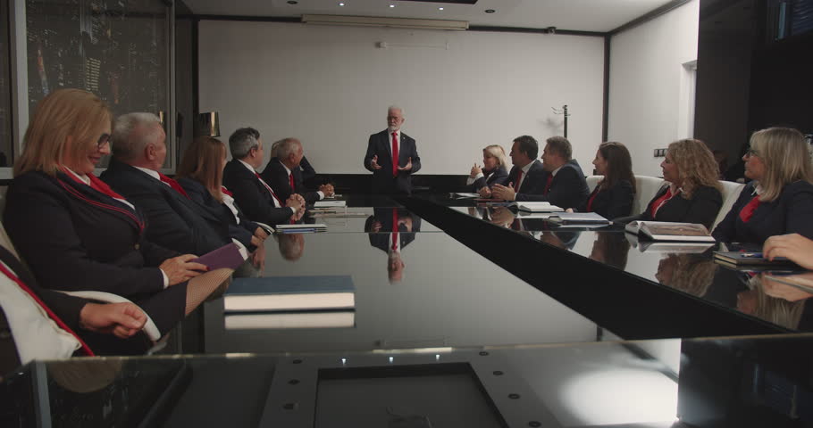 In a corporate boardroom, senior managers gather to discuss critical business issues. They wear uniform outfits with red ties, presenting a unified front. Royalty-Free Stock Footage #1110081267