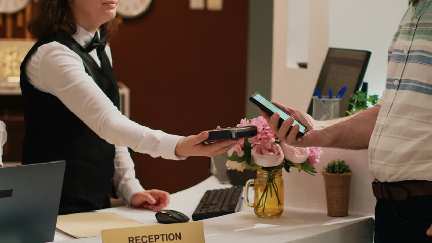 Retired guest using mobile nfc technology to pay for all inclusive room on vacation. Senior man putting smartphone next to pos terminal, electronic payment on retirement trip. Handheld shot.