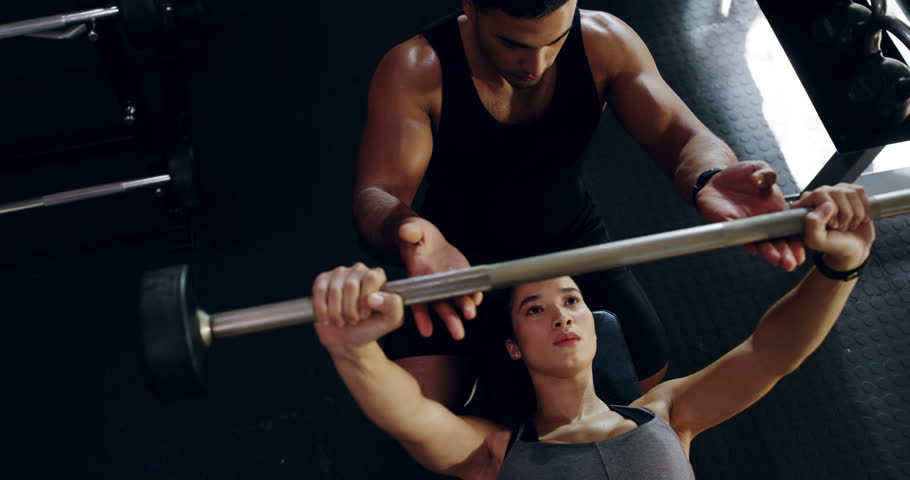 Coach, man and woman with weightlifting, bench press or motivation with personal trainer, fitness or help at gym. Training commitment, barbell and exercise with bodybuilder, challenge and support