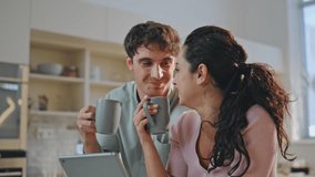 Family drinking coffee with tablet sitting home kitchen close up. Happy smiling couple laughing enjoying morning beverage looking computer screen. Cheerful spouses watching social media together. - Powered by Shutterstock - Get 15% off with code: PIKWIZARD15