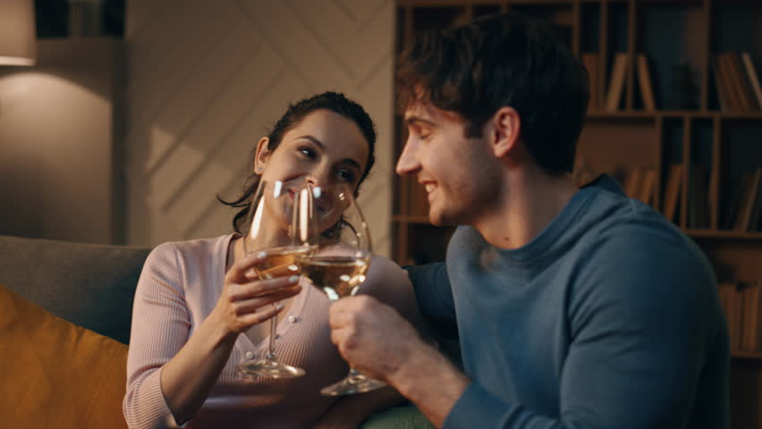 Relaxed lovers drinking wine in cozy apartment interior at night close up. Happy loving couple enjoy romantic evening at home with tasty alcohol. Smiling young spouses clinking glasses sitting couch. Royalty-Free Stock Footage #1110084053