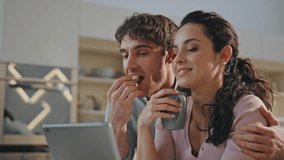 Breakfasting couple calling online using modern tablet at kitchen close up. Happy relaxed spouses talking at video meeting in apartment enjoying family morning together. Internet communication concept
