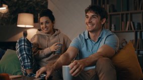 Relaxed couple watching tv show sitting comfortable couch late evening. Happy smiling spouses enjoy movie relaxing with coffee together. Loving husband hugging beautiful wife in domestic pijama. - Powered by Shutterstock - Get 15% off with code: PIKWIZARD15