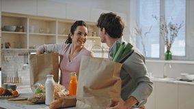 Couple putting shoppings on kitchen table arrived from grocery store close up. Smiling family unpacking eco paper packages at home cuisine. Happy spouses sorting food on countertop for cooking dinner. - Powered by Shutterstock - Get 15% off with code: PIKWIZARD15