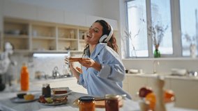 Girl preparing food in headphones singing along favorite song at cozy kitchen. Carefree joyful woman dancing listening music in headset cooking breakfast. Smiling brunette making tasty toasts alone. - Powered by Shutterstock - Get 15% off with code: PIKWIZARD15