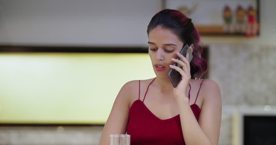 Indian thirsty tired sad depressed woman standing in modern kitchen hold glass drinking water at indoor home. Exhausted upset tense worried young female feel bad talking on mobile phone inside house | Shutterstock HD Video #1110092367