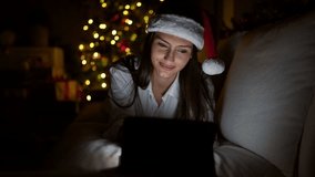 Young beautiful hispanic woman watching video on touchpad celebrating christmas at home