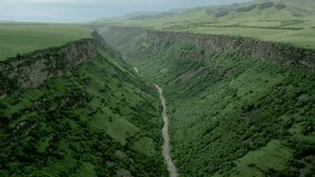 Deep rocky canyon with steep walls. At the bottom is the Dzoraget River near Gnevank Monastery in Armenia. Above is the village of Kurtan against an overcast sky. Drone video. Fly forward.