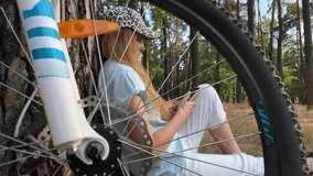 Bicycle wheel. The girl is holding a smartphone and watching a video. View of a woman through a bicycle wheel. A cyclist shares his weekend trip with friends. Vacation. Summer day. High quality 4k