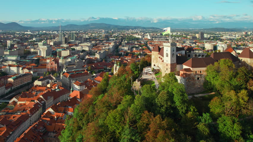 Aerial view of the Ljubljana old town, Slovenia. Ljubljana castle, historic buildings and Ljubljanica river in Slovenian capital at sunny day. Beautiful mountain range at background Royalty-Free Stock Footage #1110104827