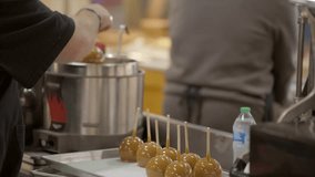 This video shows fresh apples being dipped into a pot of caramel, making candied apples on sticks for customers.