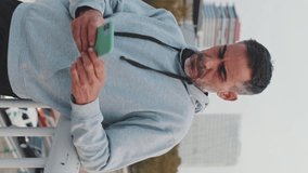Vertical video, Middle-aged man in sportswear uses mobile phone while standing on bridge