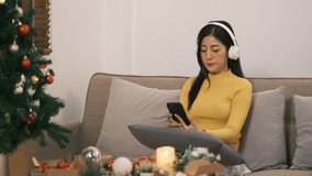 Smiling woman with headphones listening to music, relaxing on sofa in Christmas living room - Powered by Shutterstock - Get 15% off with code: PIKWIZARD15