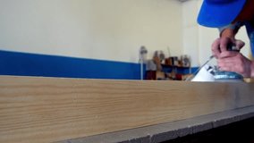 Slow motion video. Carpenter processes wooden bar on workbench in carpentry shop. View of worker's hands with power tools. Carpenter grinds wooden board. Close-up. Real workflow..