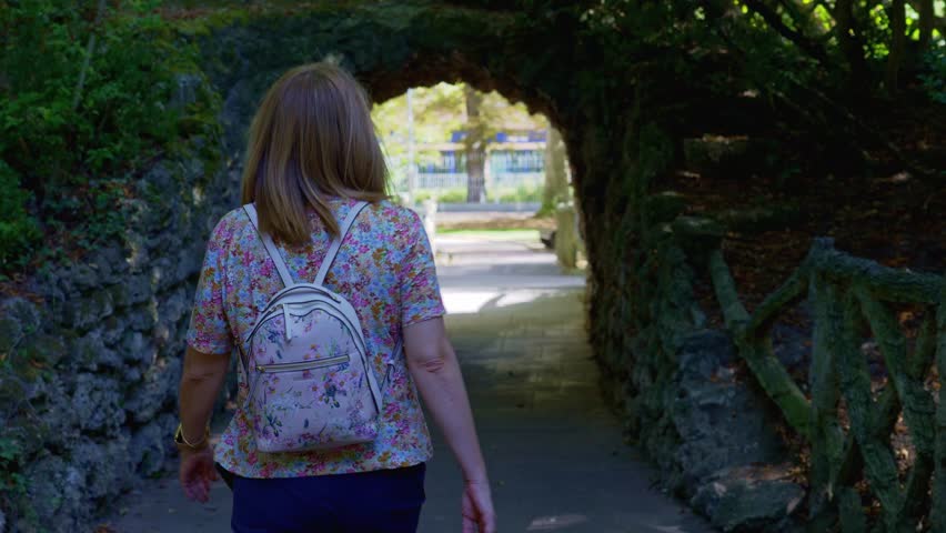 Woman strolling through a public park in a stone tunnel that forms an arch, Vitoria, Spain.