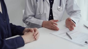 Doctor and patient sitting at the table and discussing something. The pediatrician in a blue dotted blouse and white medical coat is gesturing actively. Medicine concept.