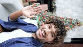 POV Webcam view Vertical video. Young man talking on a video call using a smartphone sitting at home during winter New Year Christmas holidays. Smiling happy male talking wishes congratulates remotely - Powered by Shutterstock - Get 15% off with code: PIKWIZARD15