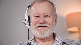 portrait of an elderly old man with a microphone and headphones talking on video call on a laptop, looking at camera