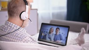 remote communication, an elderly man using a headset has a video conversation on a laptop while sitting on sofa in room