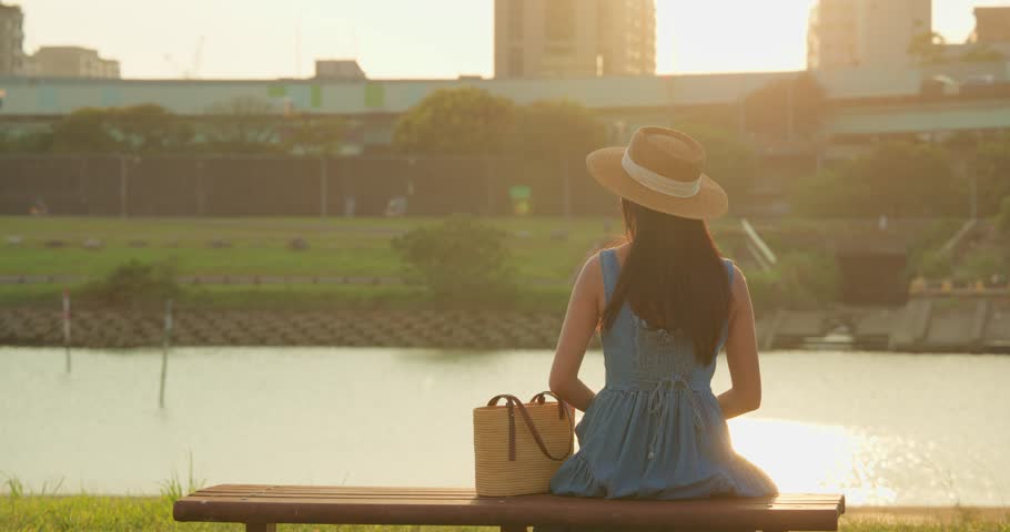 Woman sit the bench under the sunset at river park
